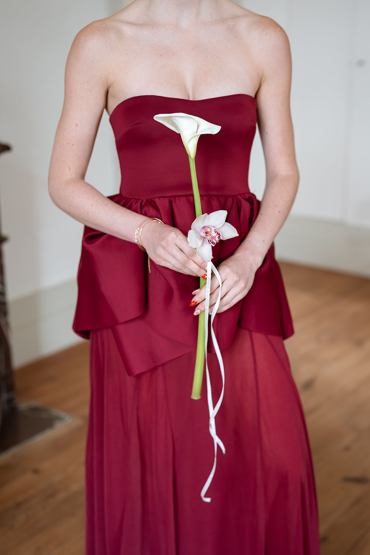 Bridesmaid in a burgundy strapless gown holding a single calla lily