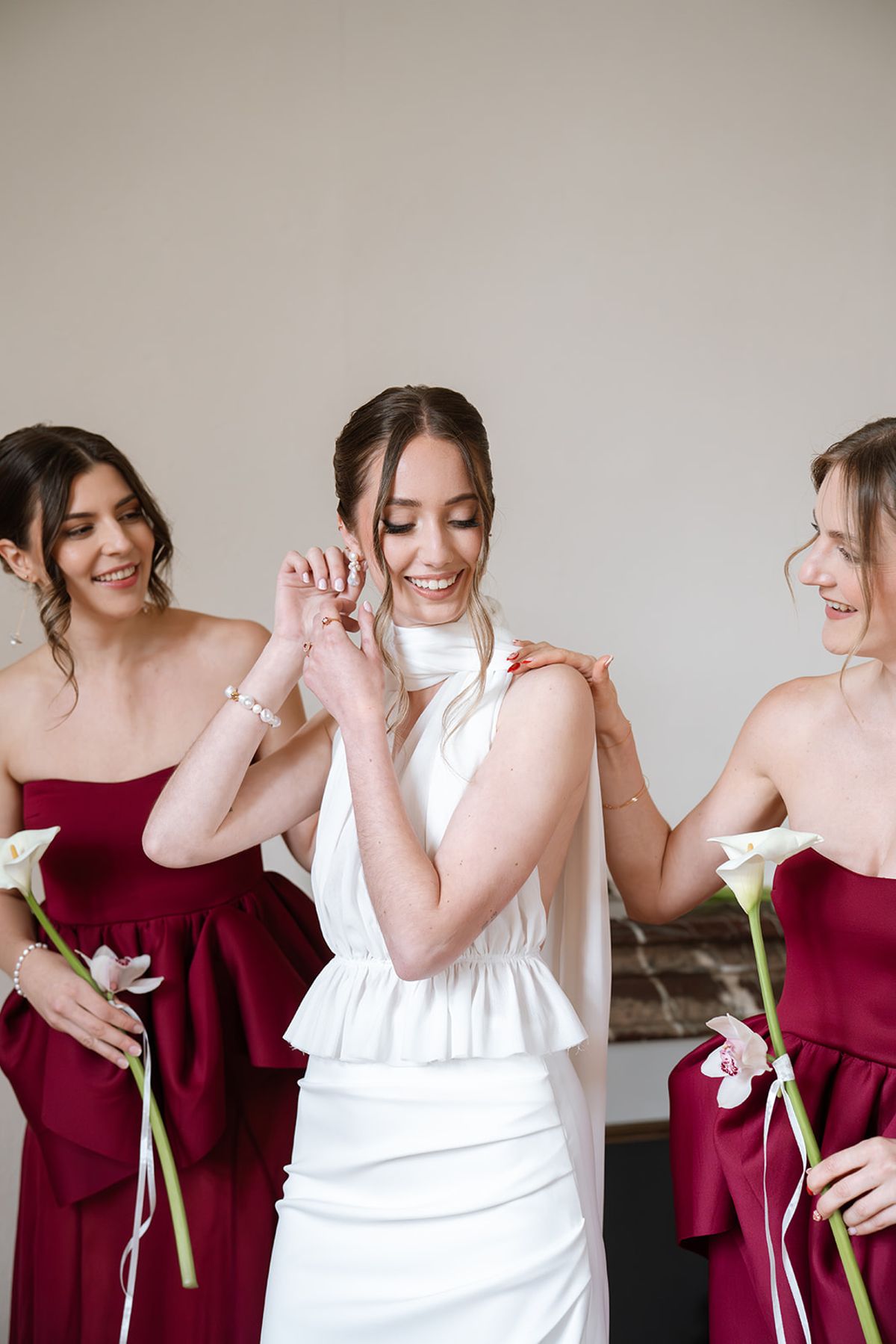 Bride touching her earring as two bridesmaids in burgundy laugh beside her