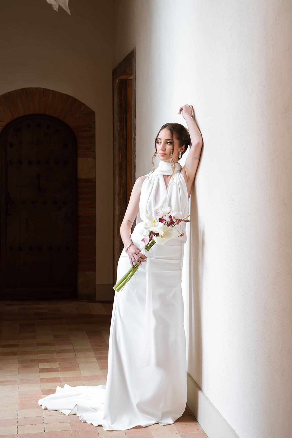 Bride leaning against a white wall with her bouquet