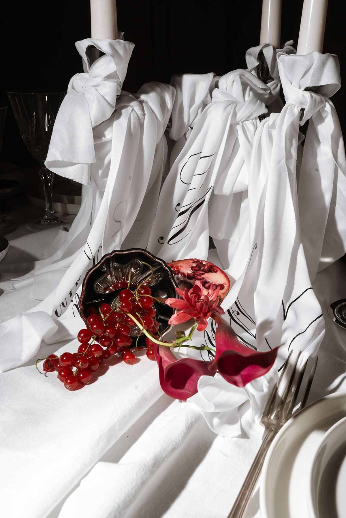 Candles wrapped in white fabric with pomegranates and red currants