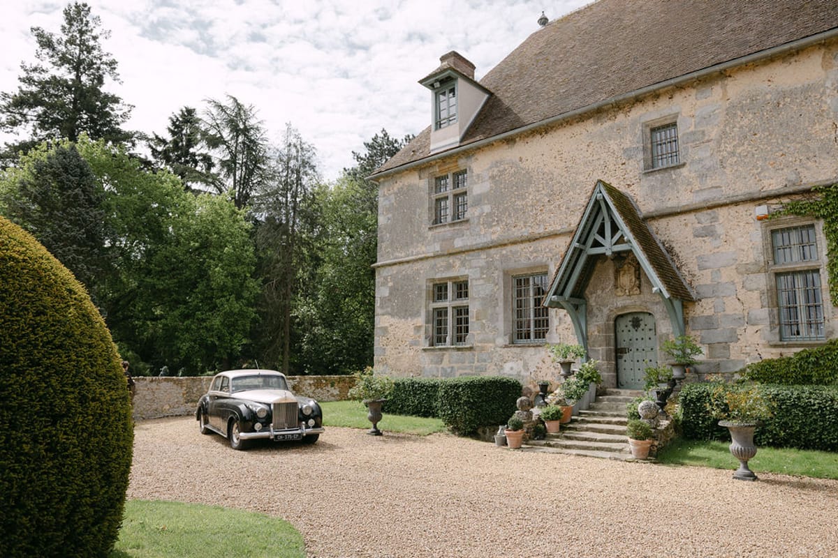 Manoir de Vacheresses' stone exterior and driveway with a vintage car parked outside, late spring.