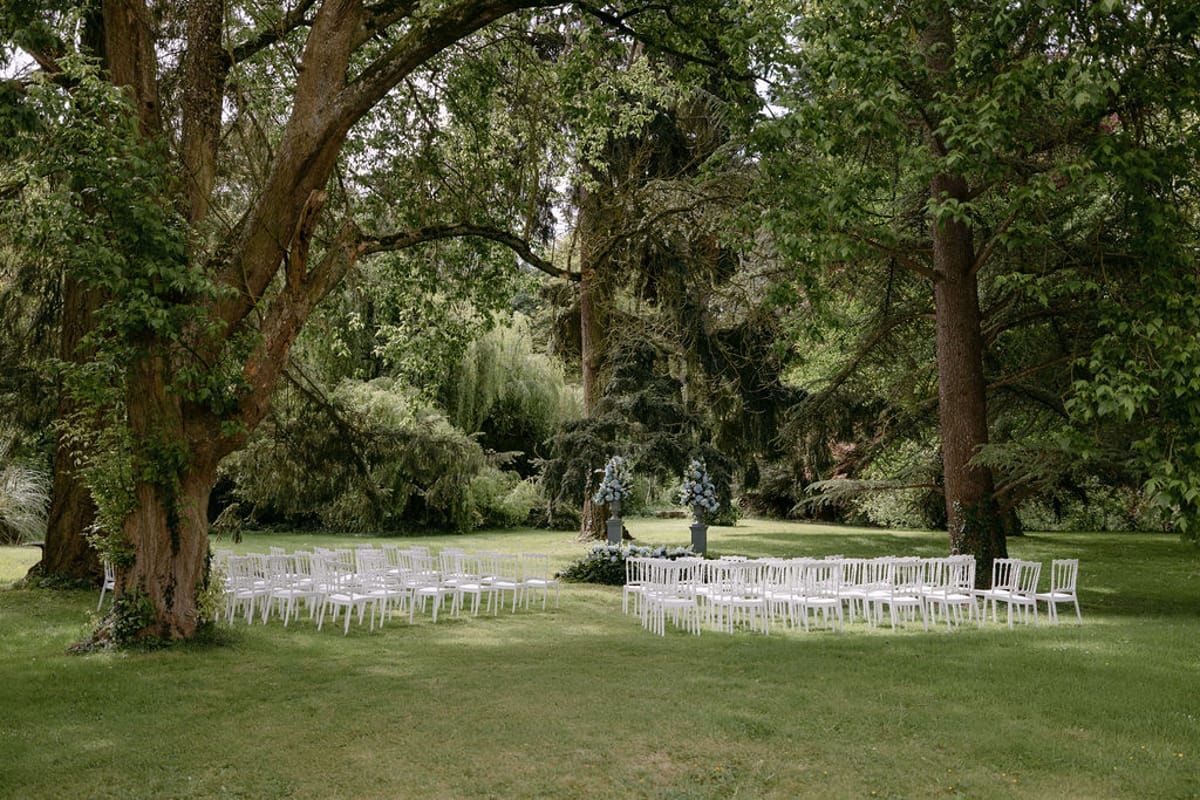 Rows of empty white chairs set for the ceremony beneath tall trees at Manoir de Vacheresses.