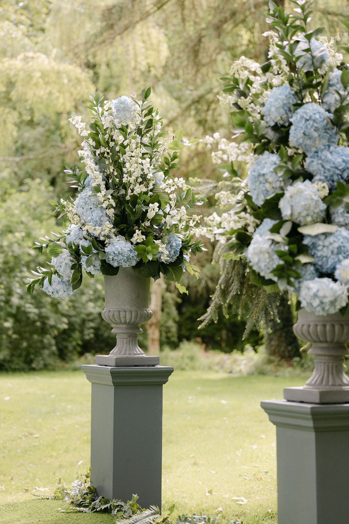 Blue hydrangea and white floral arrangement in a stone urn at the ceremony space.