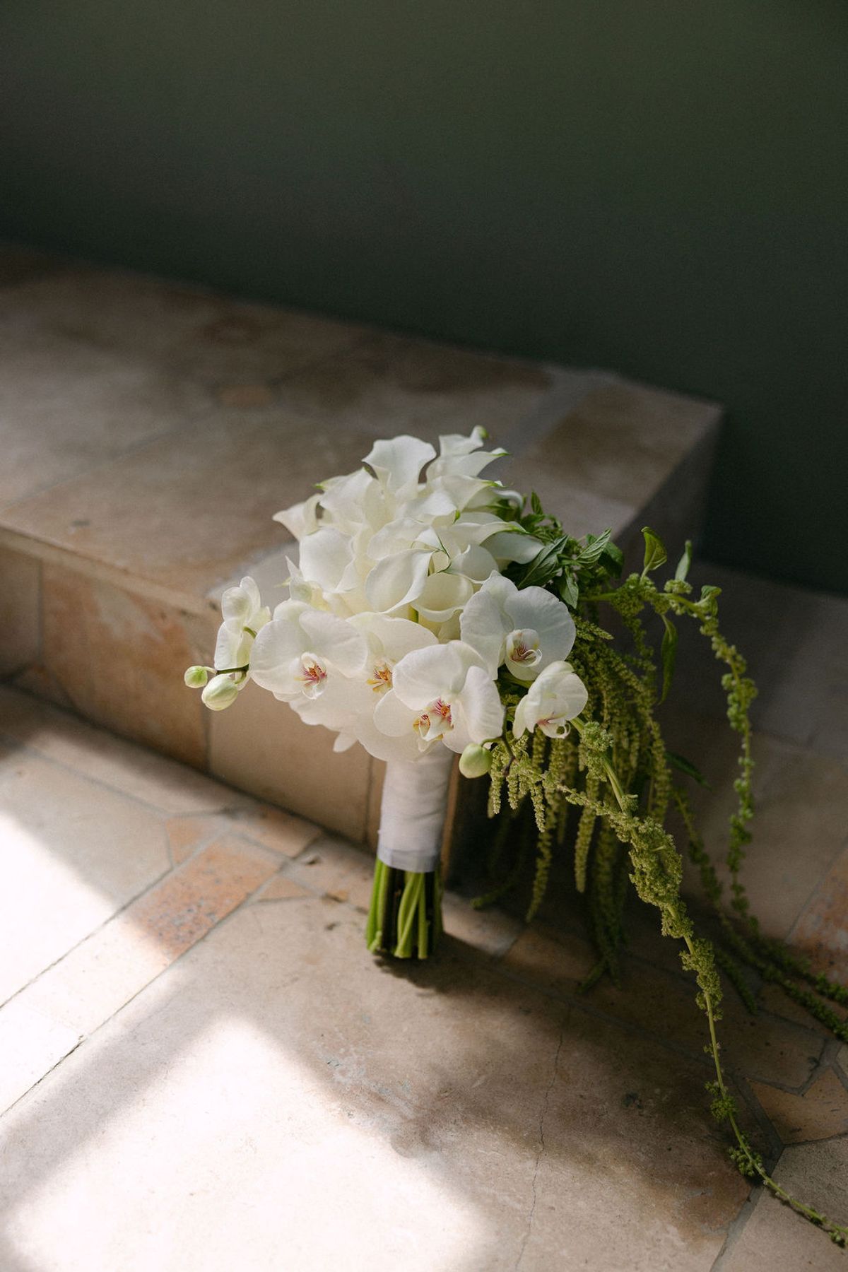 White calla lily and orchid bridal bouquet resting on a stone ledge.