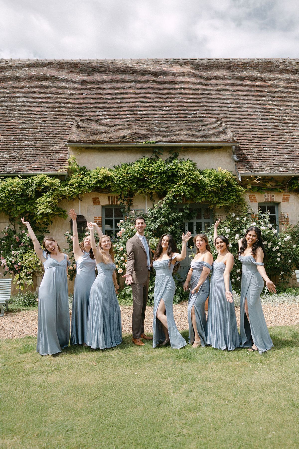 The bridal party in dusty-blue dresses and suits, group portrait on the gravel drive.