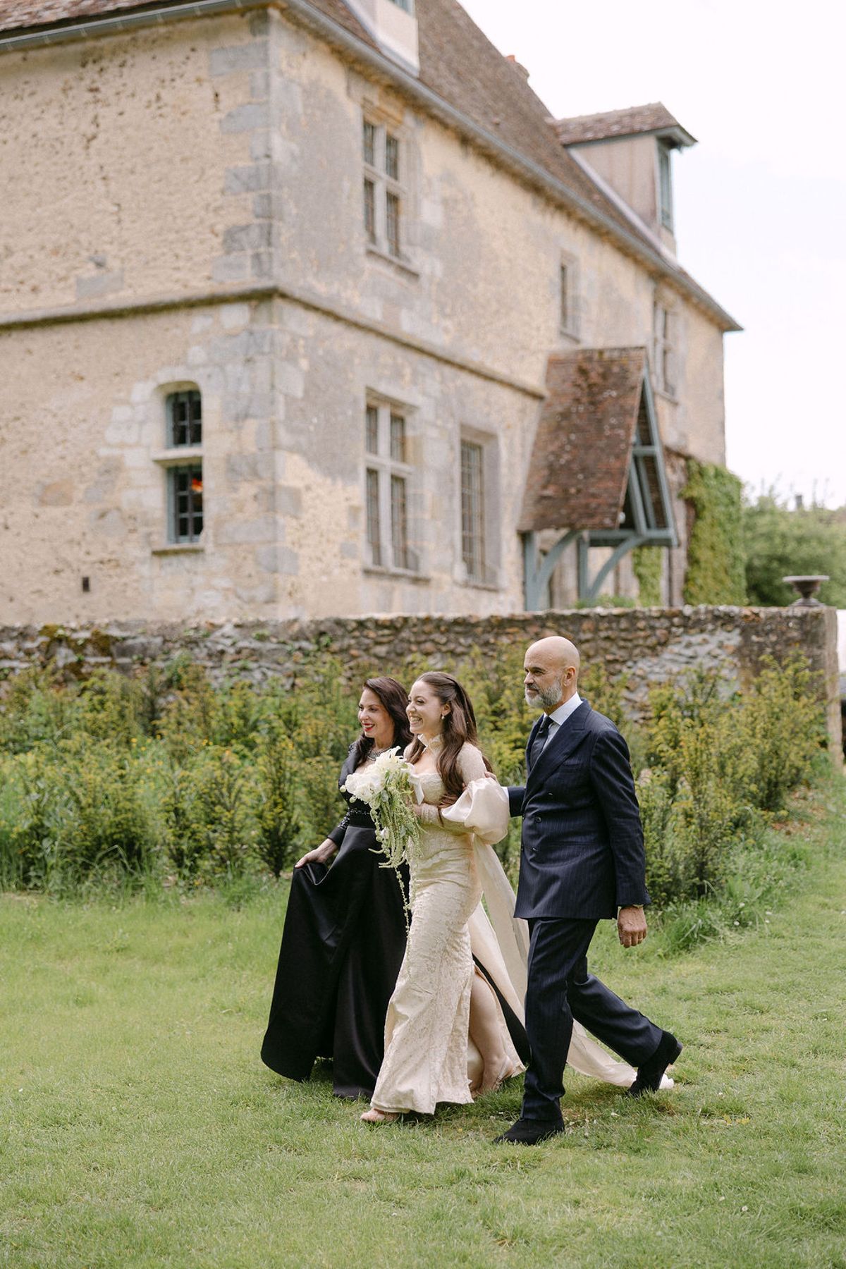 Two bridesmaids walking together in front of the manor's stone facade.
