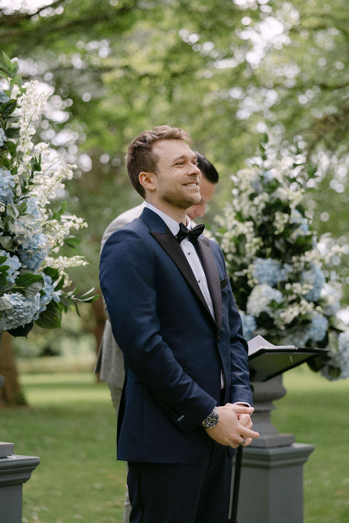 Jonathan smiling during the ceremony, floral installation visible behind him.