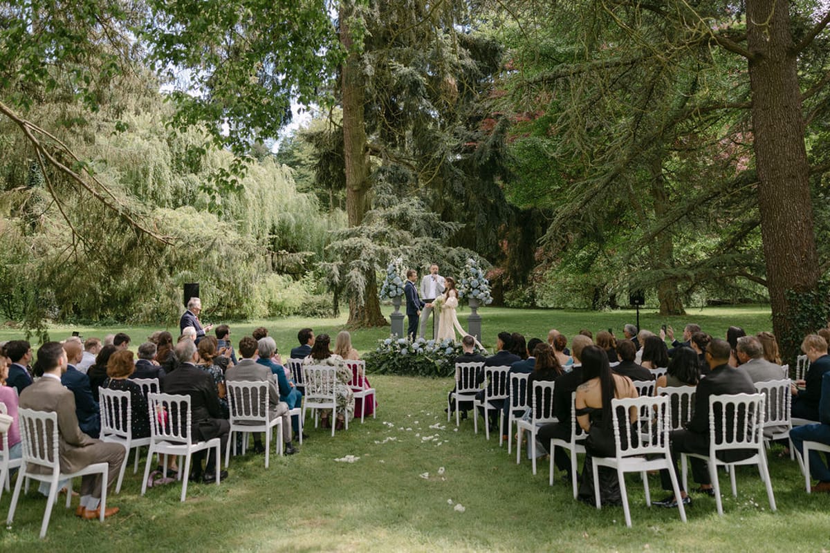 Wide view of the outdoor ceremony in progress, guests seated either side of the aisle.