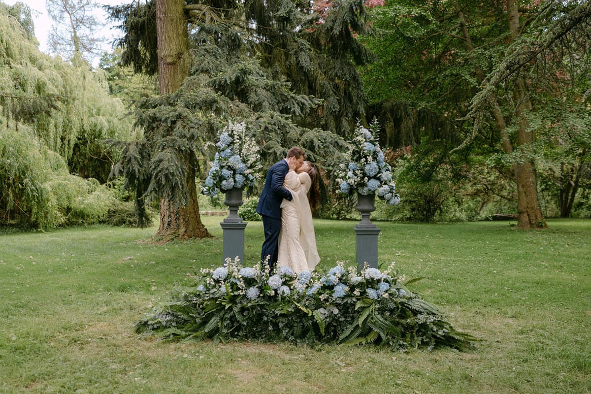 Olivia and Jonathan kissing at the altar beneath a floral arch.