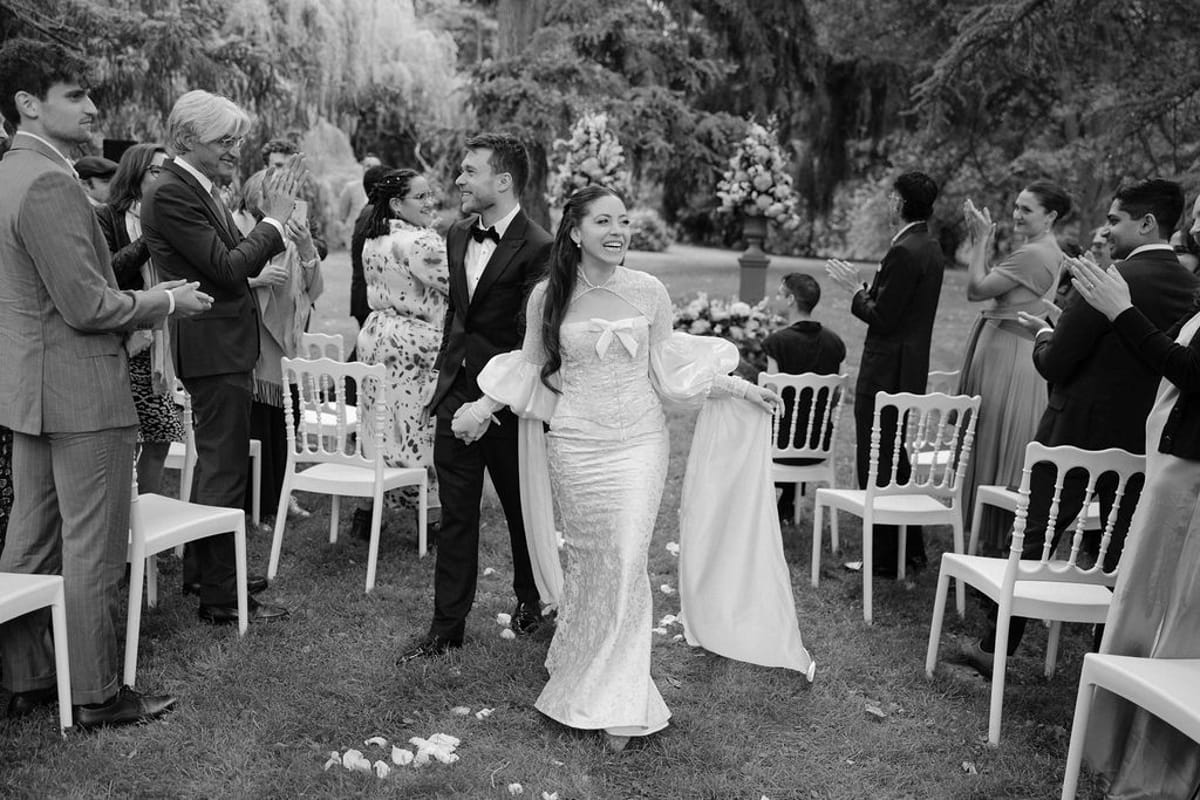 Olivia and Jonathan walking back down the aisle past applauding seated guests, black and white.