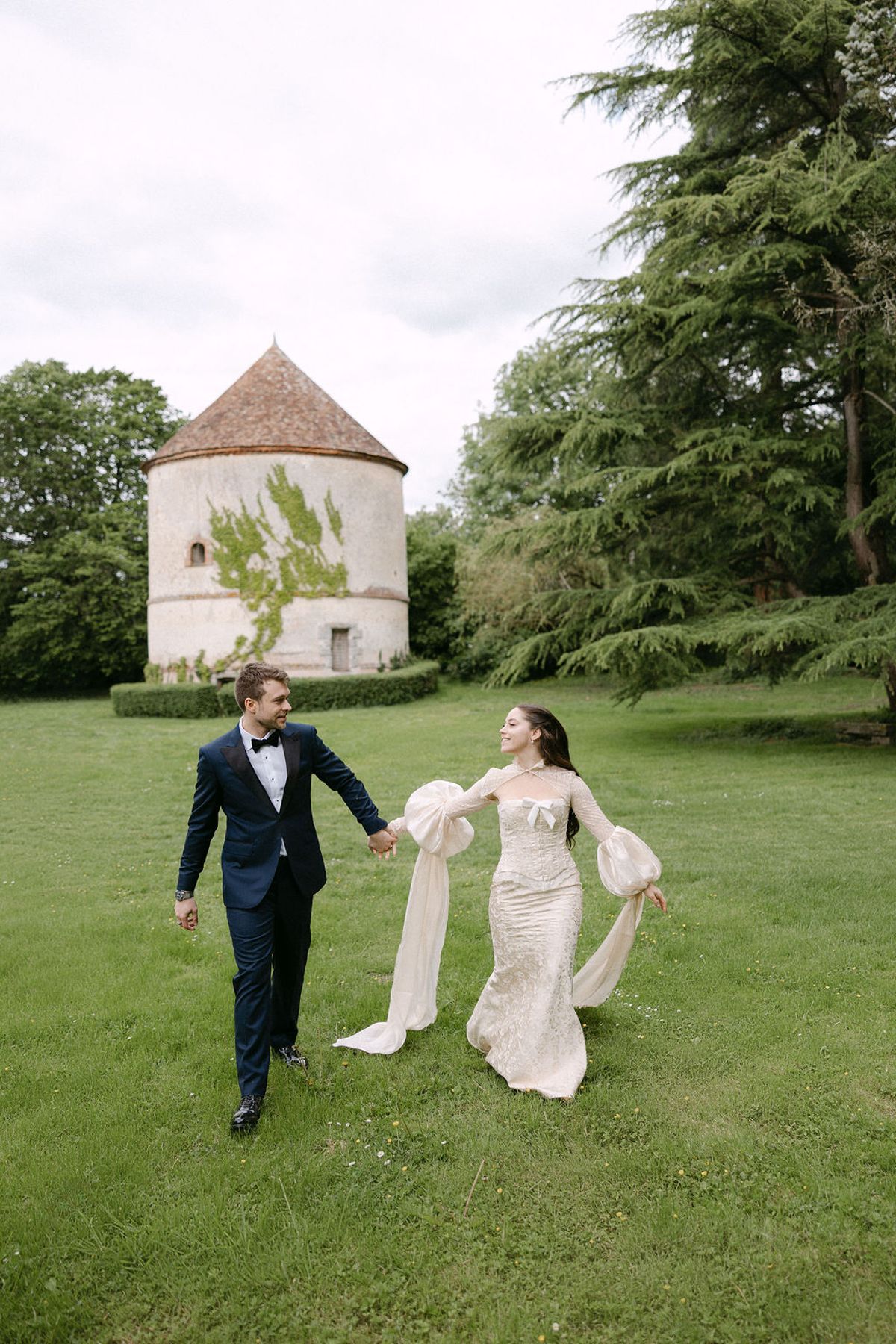 Olivia and Jonathan walking hand in hand past the manor's round tower.