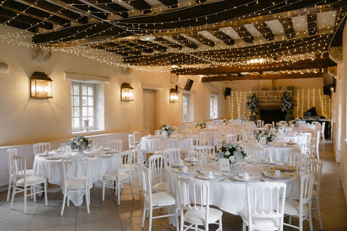 The reception room set for dinner, tables dressed in white beneath string lights.