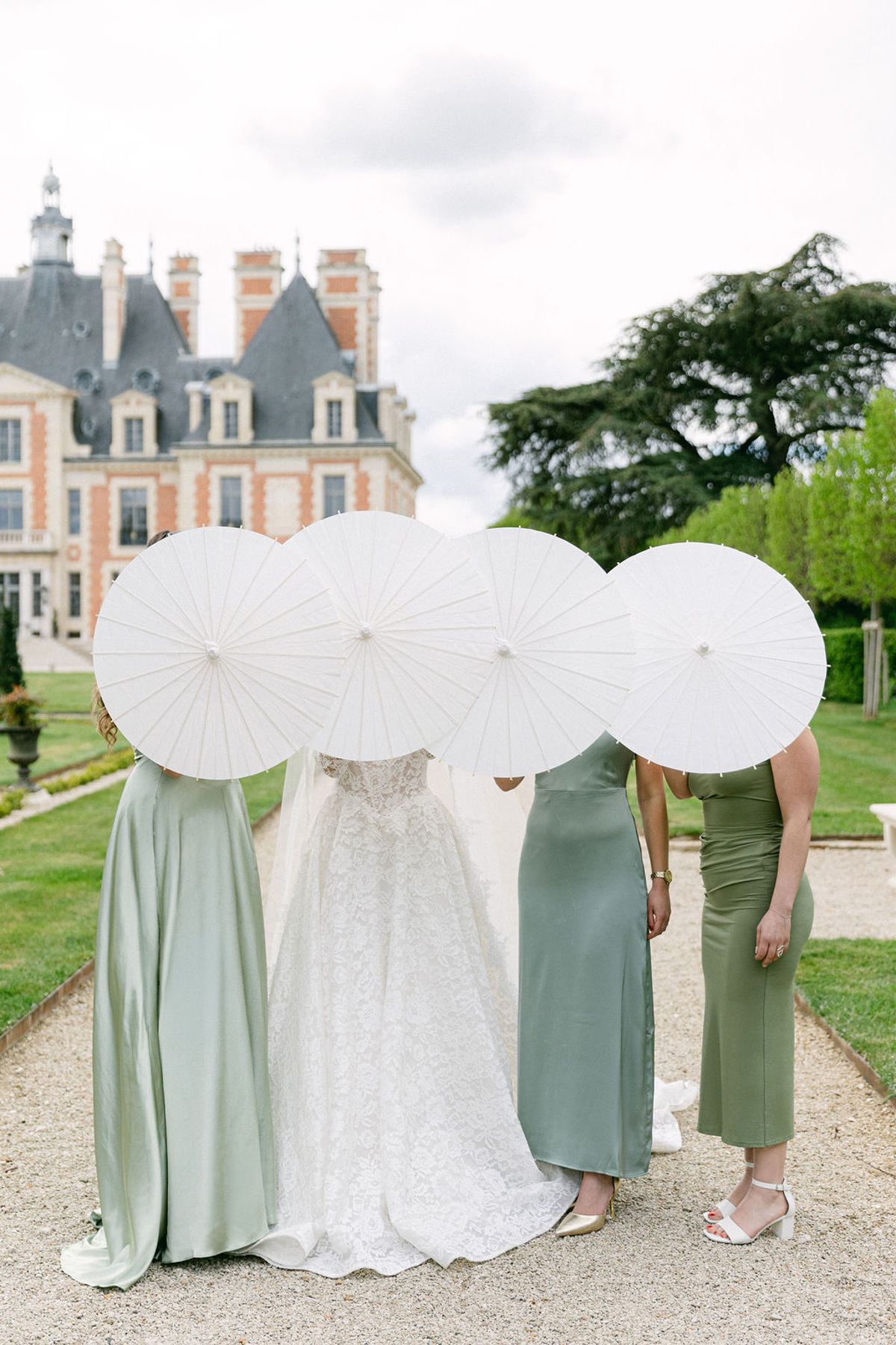 Bride and bridesmaids seen from behind under white parasols on the lawn