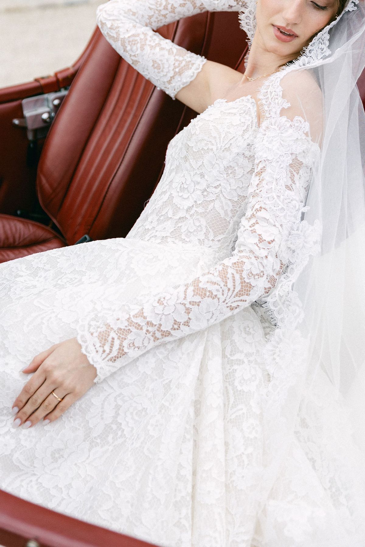 Bride reclines across the red leather seats of the open vintage car