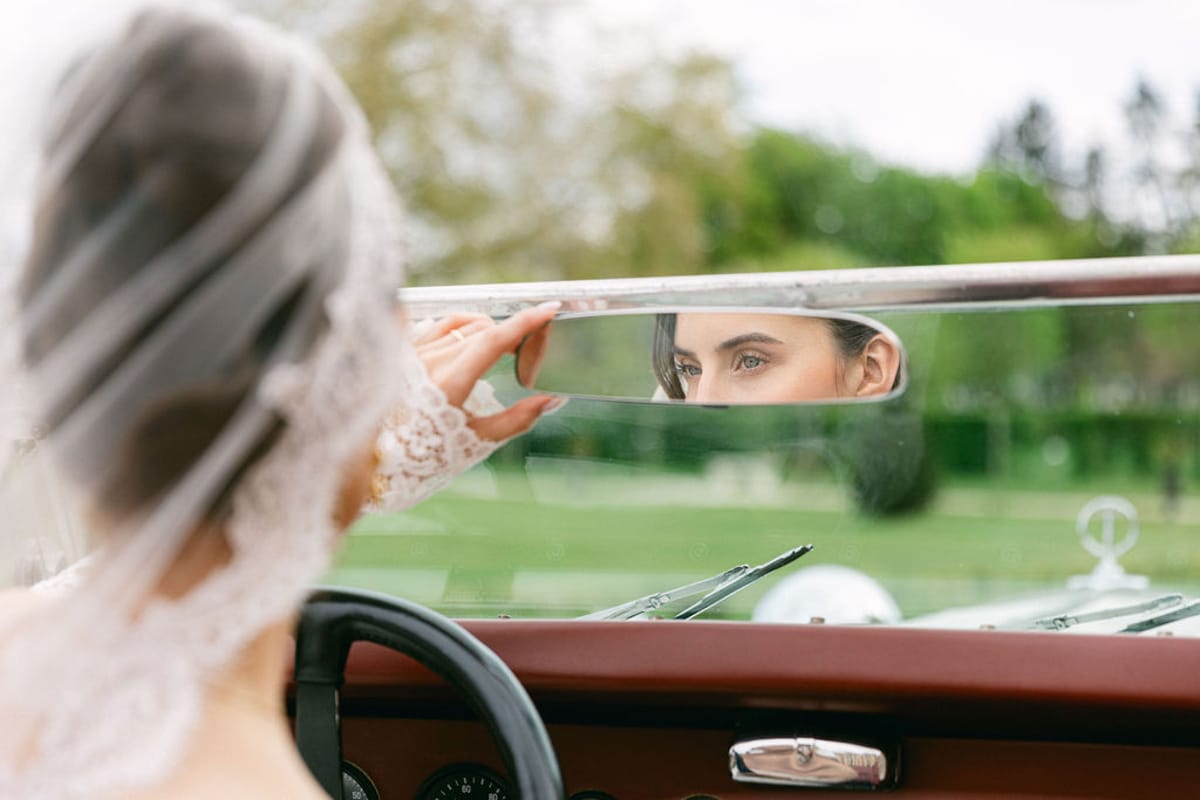 Bride in a veil looks over the wheel of the open vintage car