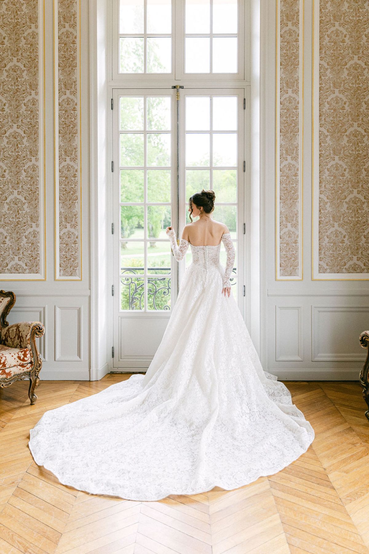Bride stands with her train laid out across the parquet of a chateau salon