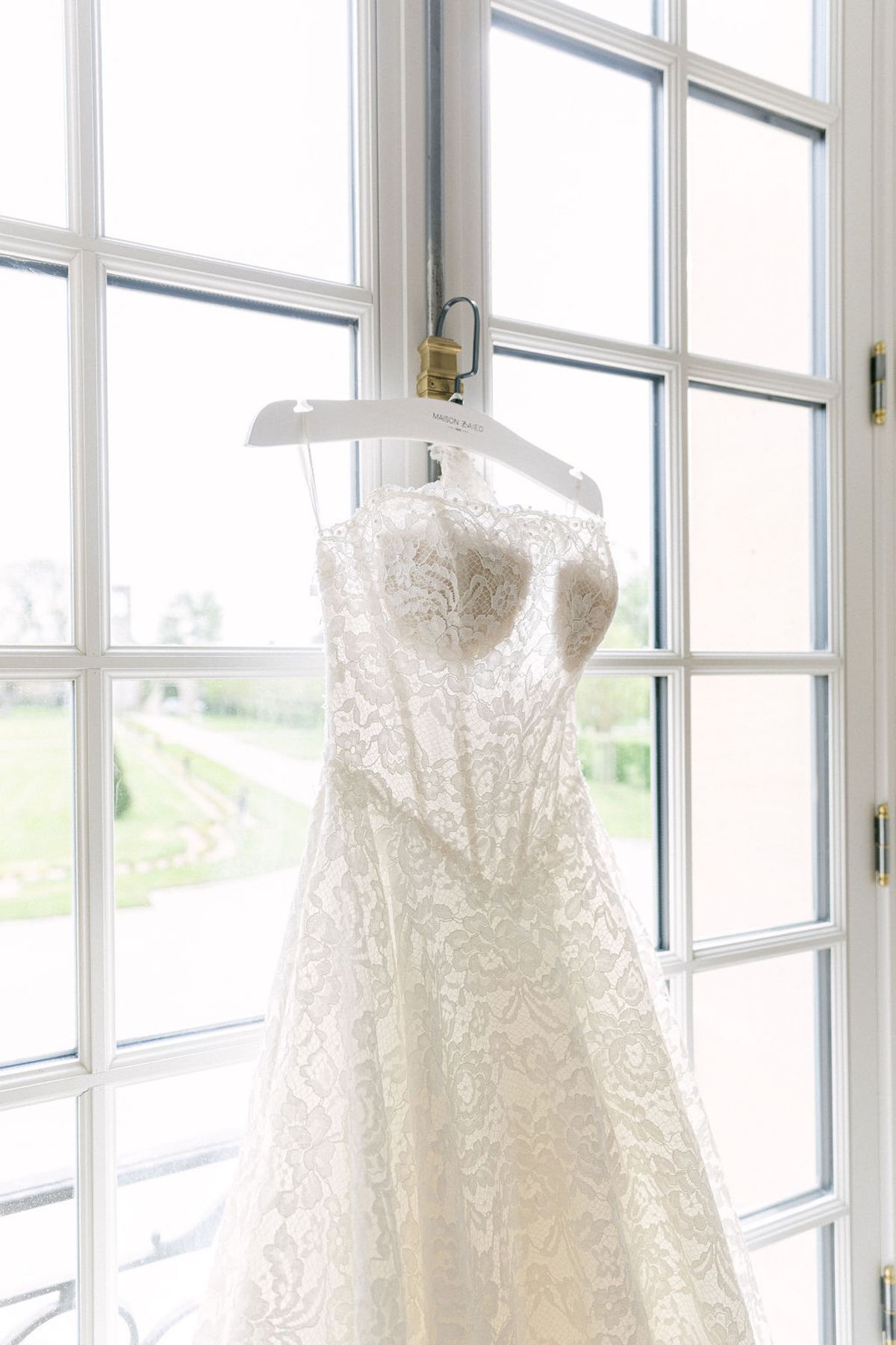 The lace wedding gown hanging in a tall window of the chateau