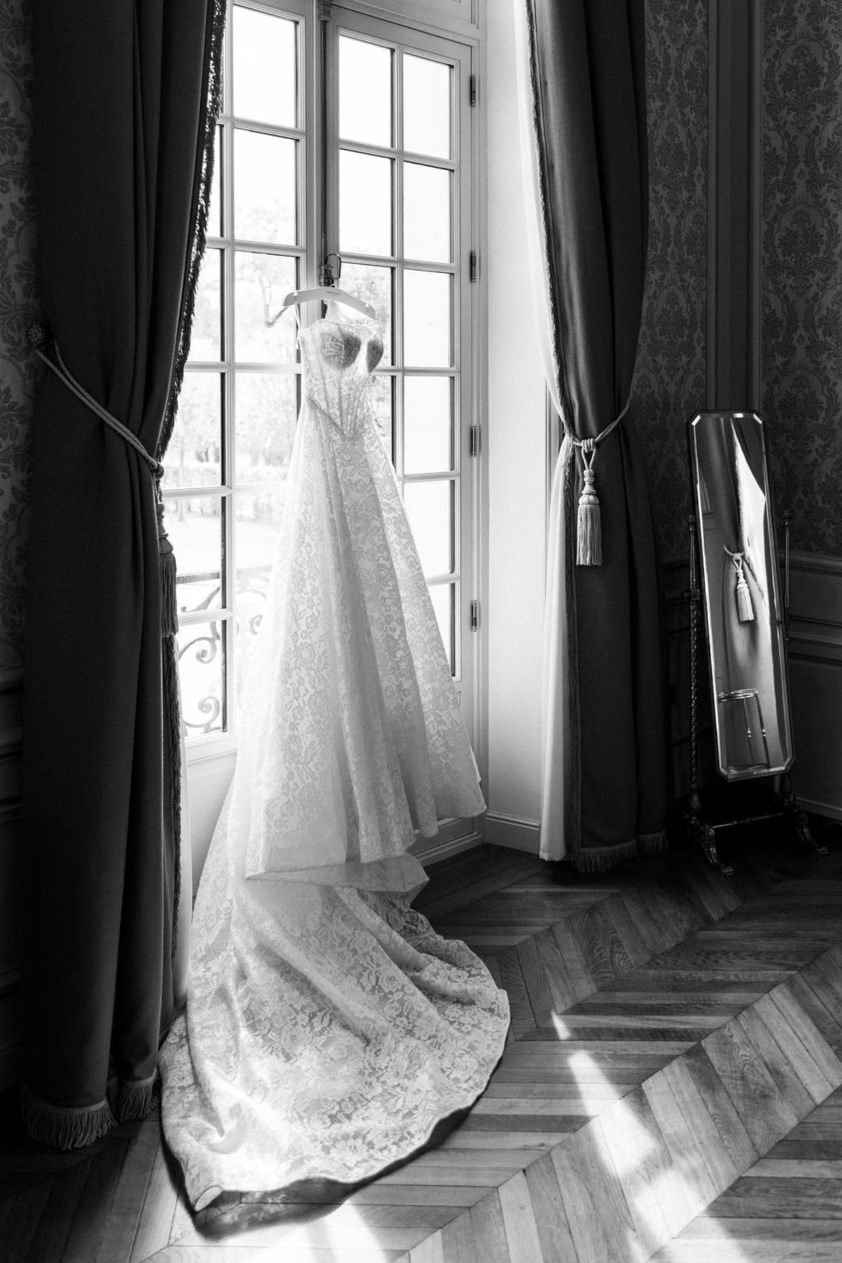 The wedding gown hanging in a tall chateau window, in black and white