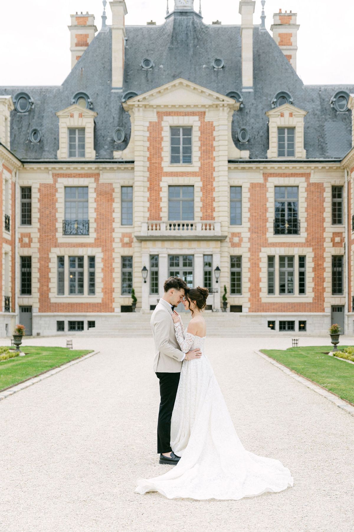 Couple embrace on the central gravel path with the chateau behind them
