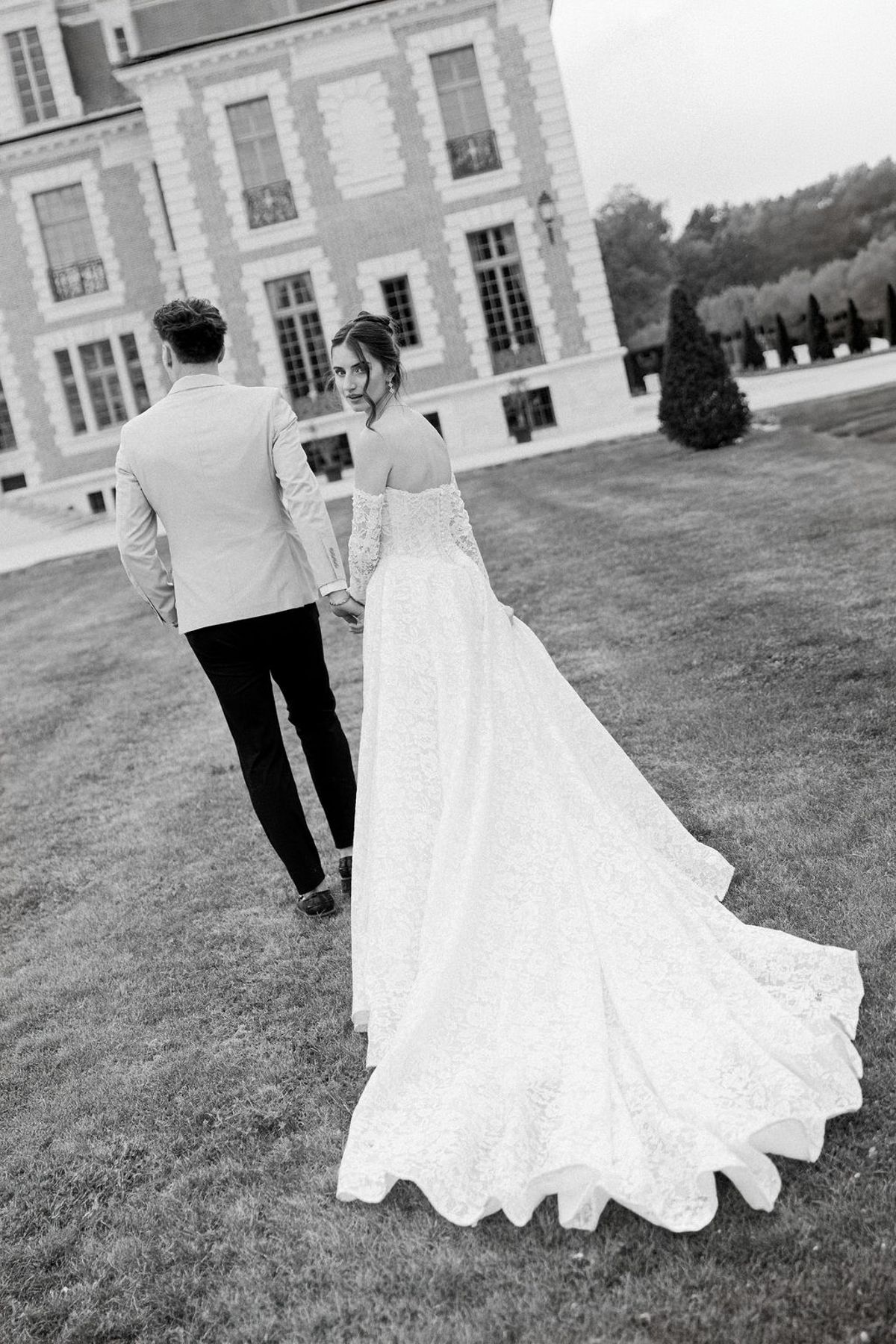 Couple walking on the lawn in black and white, the bride's train trailing behind