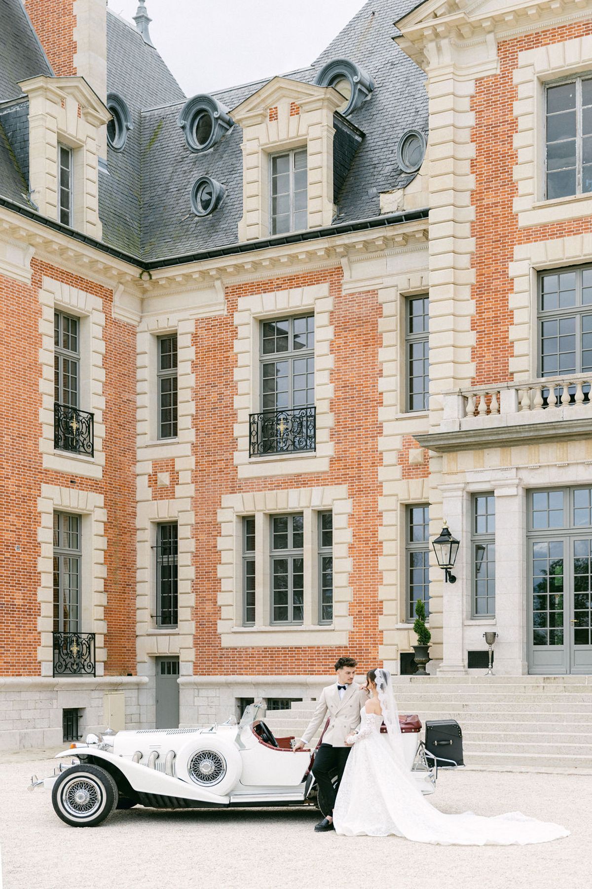 Couple in front of the chateau with the vintage car parked to one side