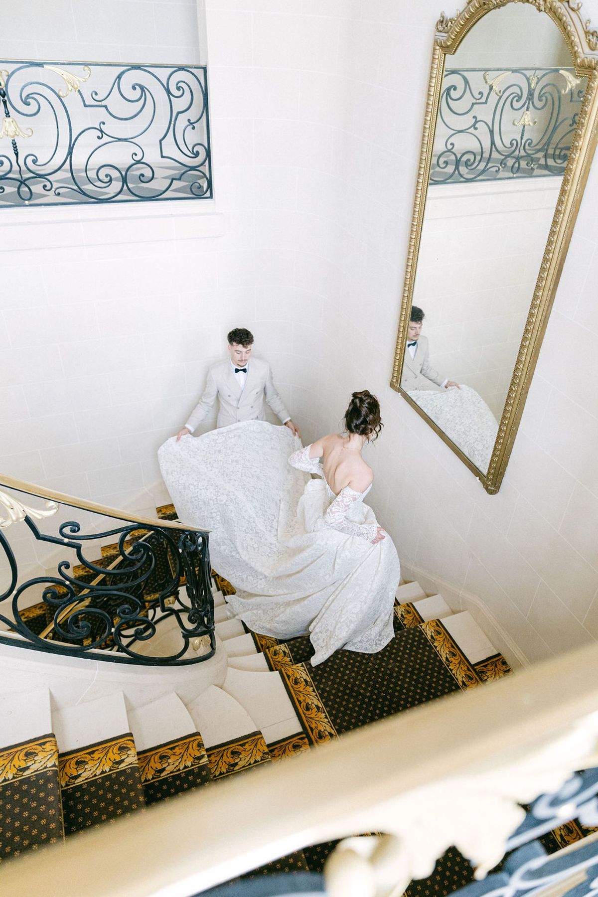 Couple beside the gilt mirror at the foot of the stairs, seen over the iron banister