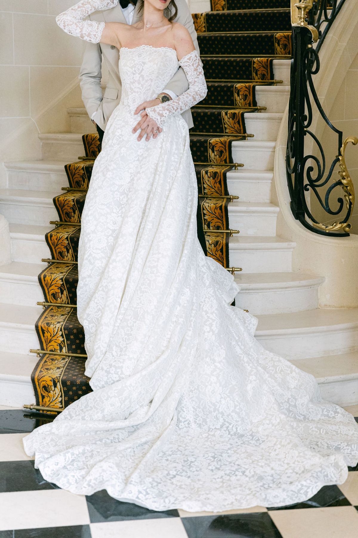 Bride's lace gown and train spill down the chateau's iron-railed staircase
