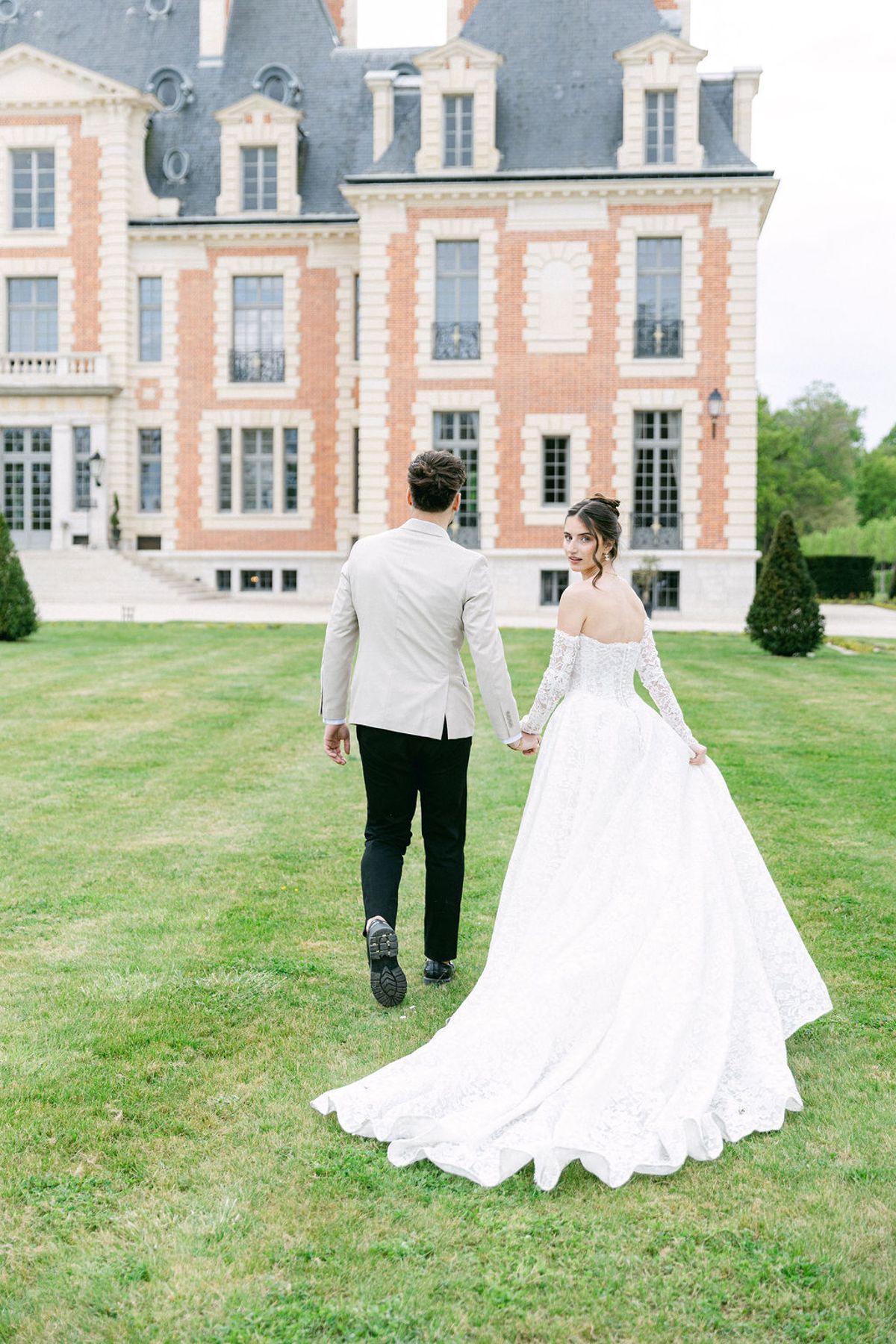 Couple walk away hand in hand across the lawn towards the chateau