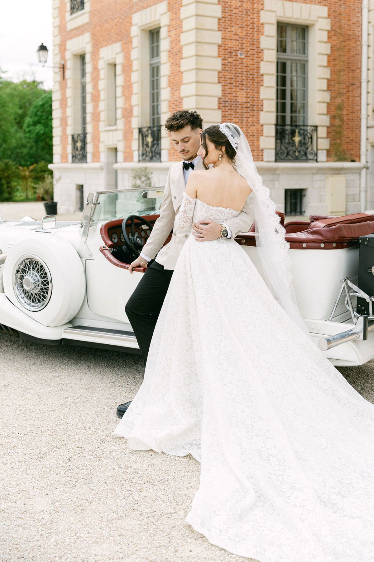 Couple kiss beside the open vintage car on the chateau drive
