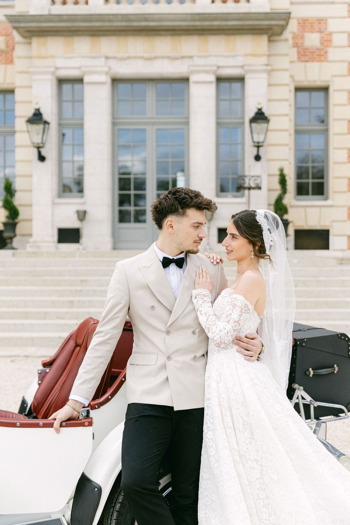 Couple embracing beside the vintage car at the foot of the chateau steps