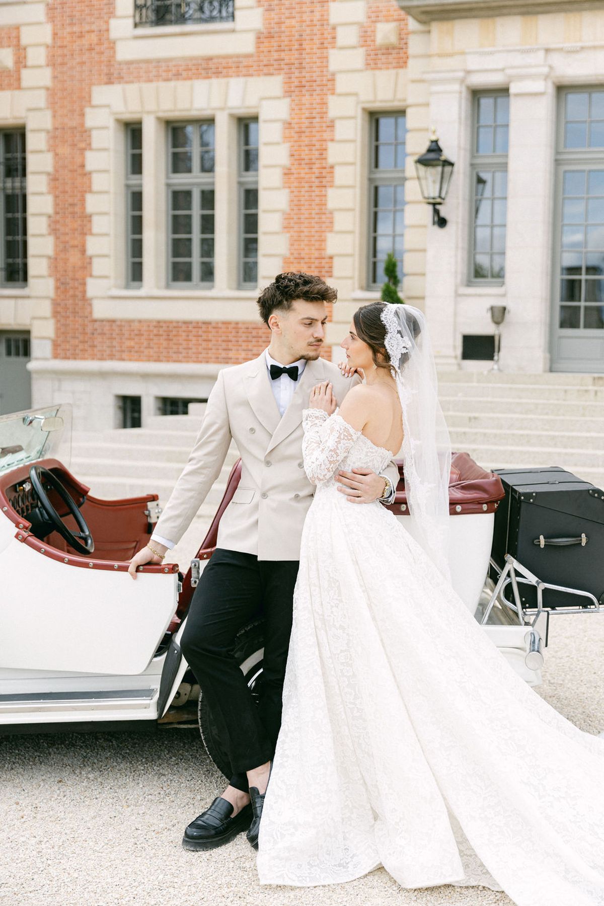 Couple facing each other beside the open vintage car in front of the chateau