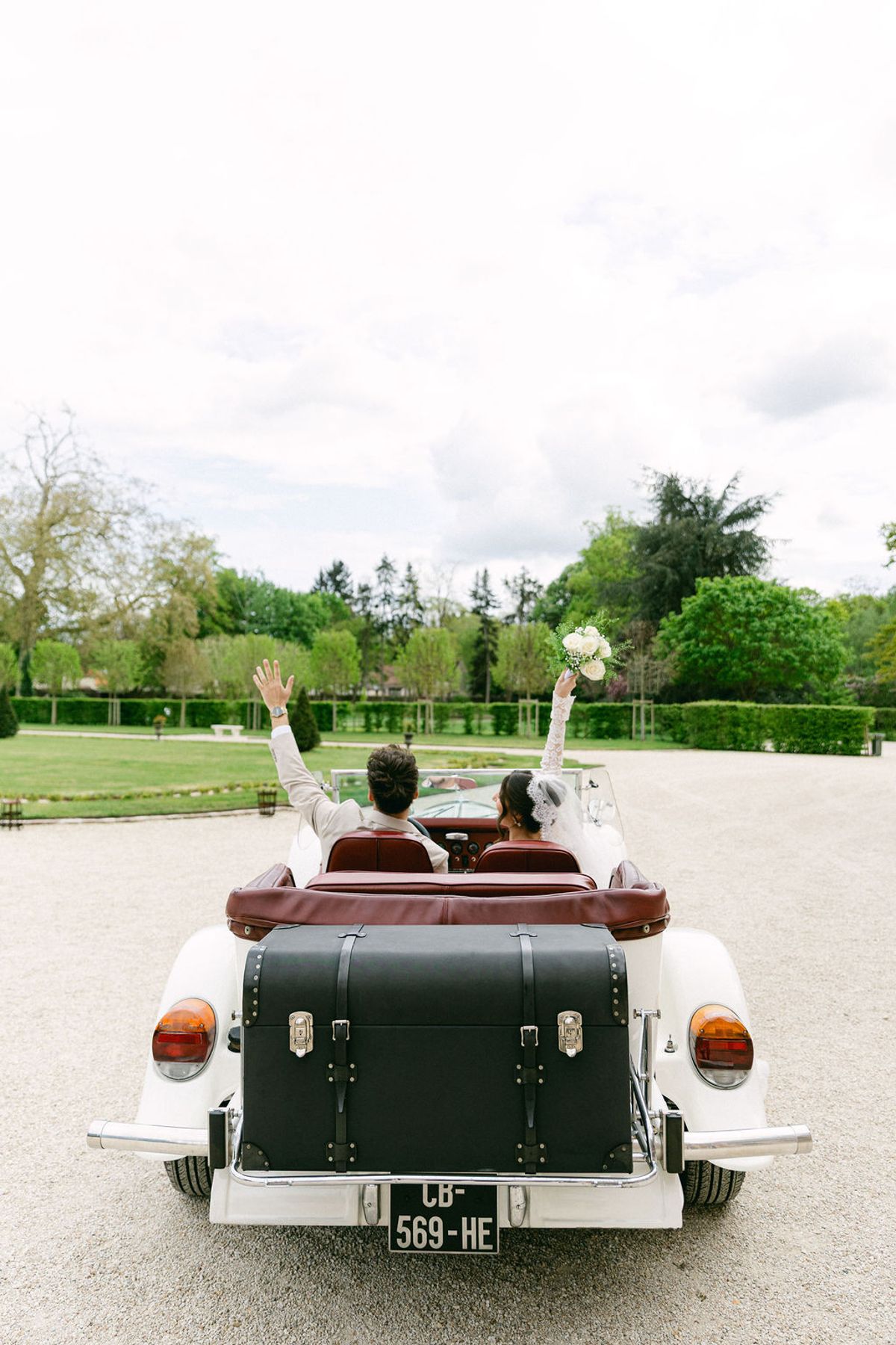 Couple raise their arms in the back of the vintage car as it pulls away
