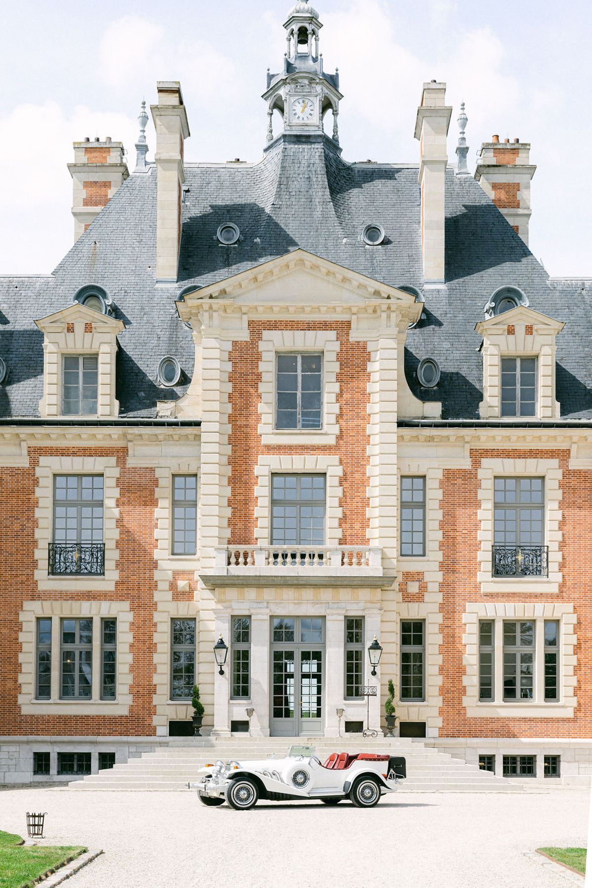 Full height of the chateau facade with the white vintage car small on the gravel below