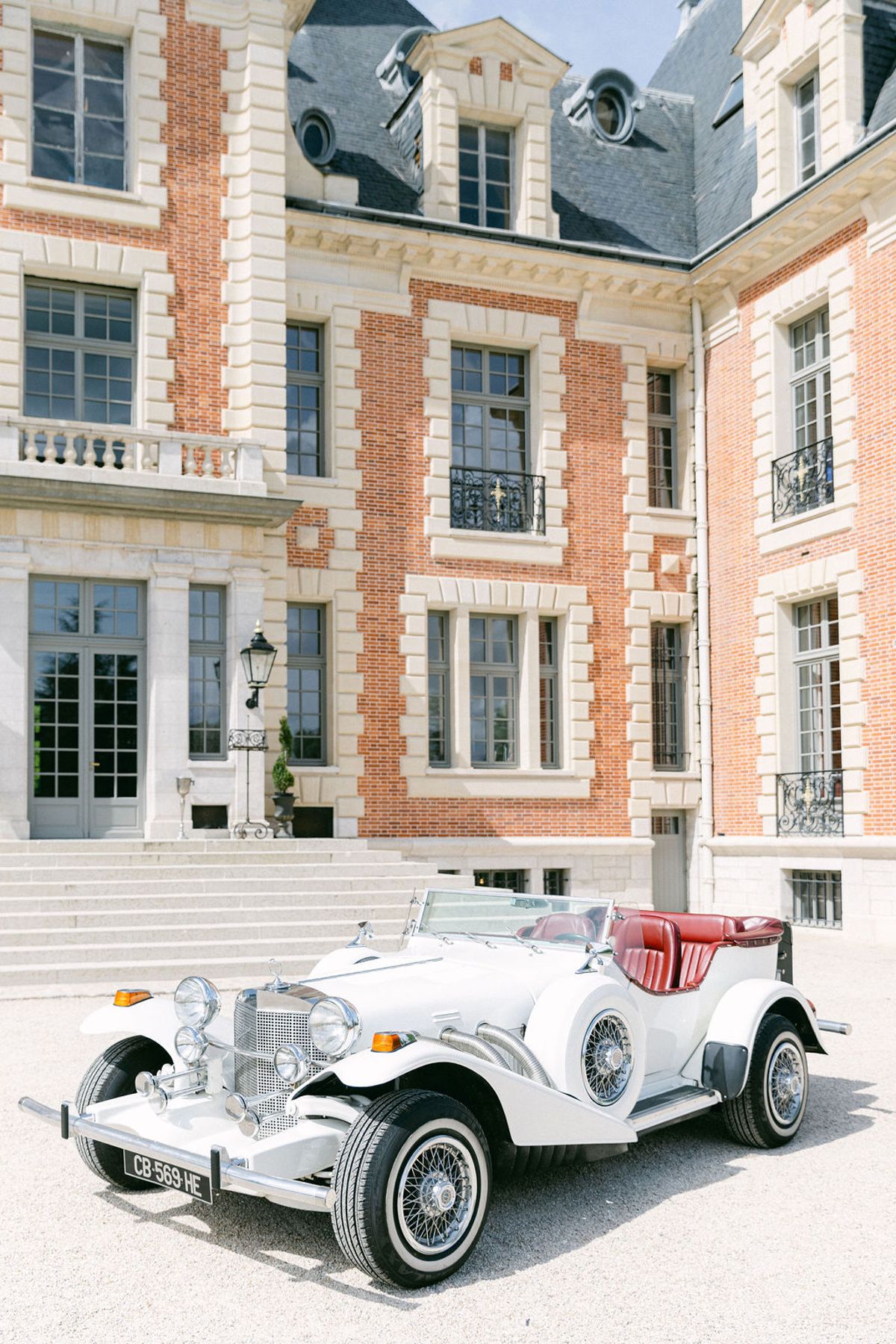 White vintage car parked on the gravel in front of the chateau facade