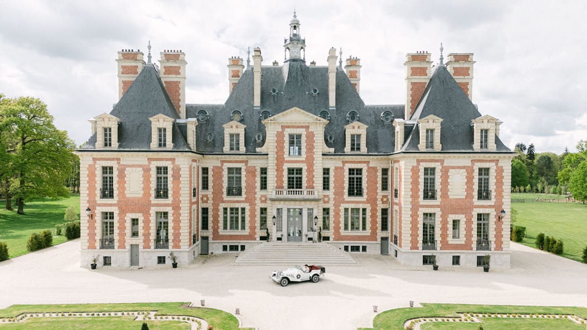 Front elevation of Chateau de Nainville-les-Roches with a white vintage car on the gravel