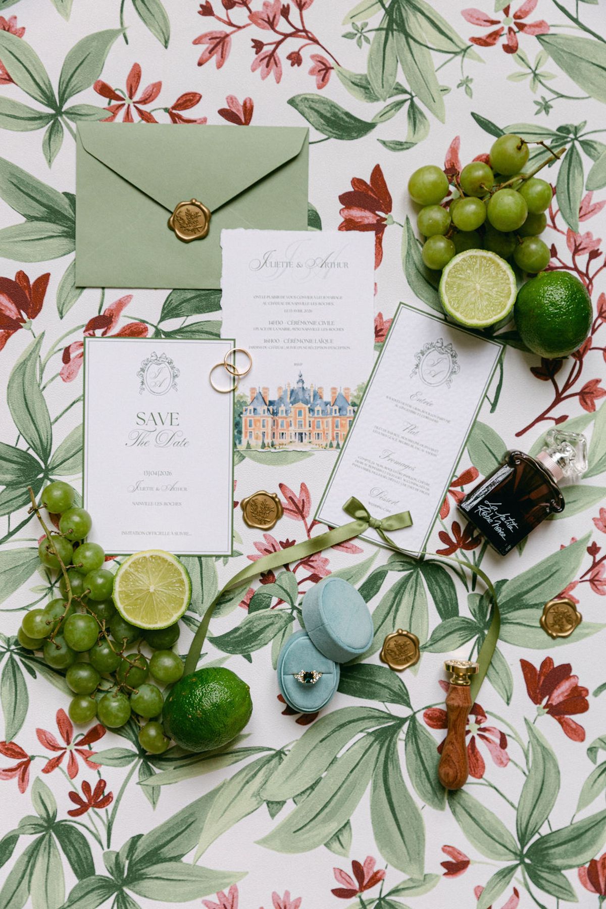 Flat lay of invitations, an envelope, limes and greenery on botanical fabric