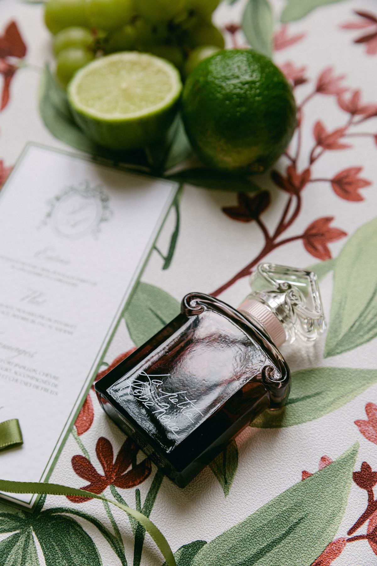 Flat lay of stationery, a glass perfume bottle, limes and botanical fabric