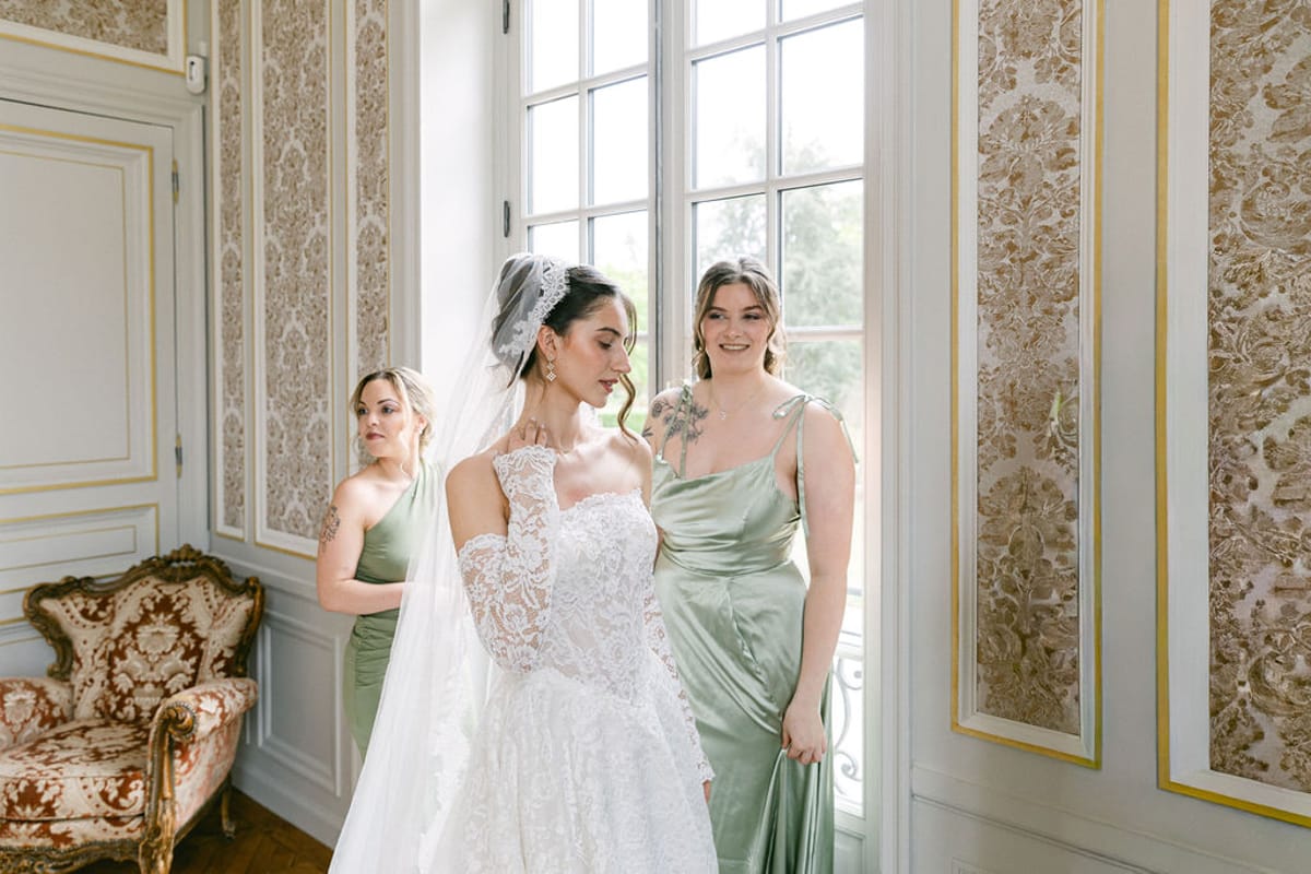 Bride and two bridesmaids in sage green in a wallpapered chateau salon