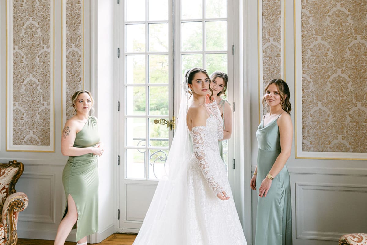 Bride in her gown between two bridesmaids at a tall salon window