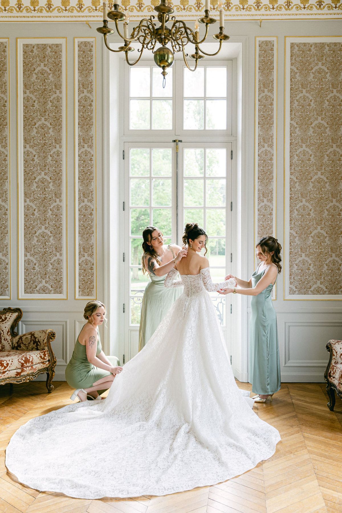 Bride with her train fanned out and three bridesmaids, one crouched at the hem