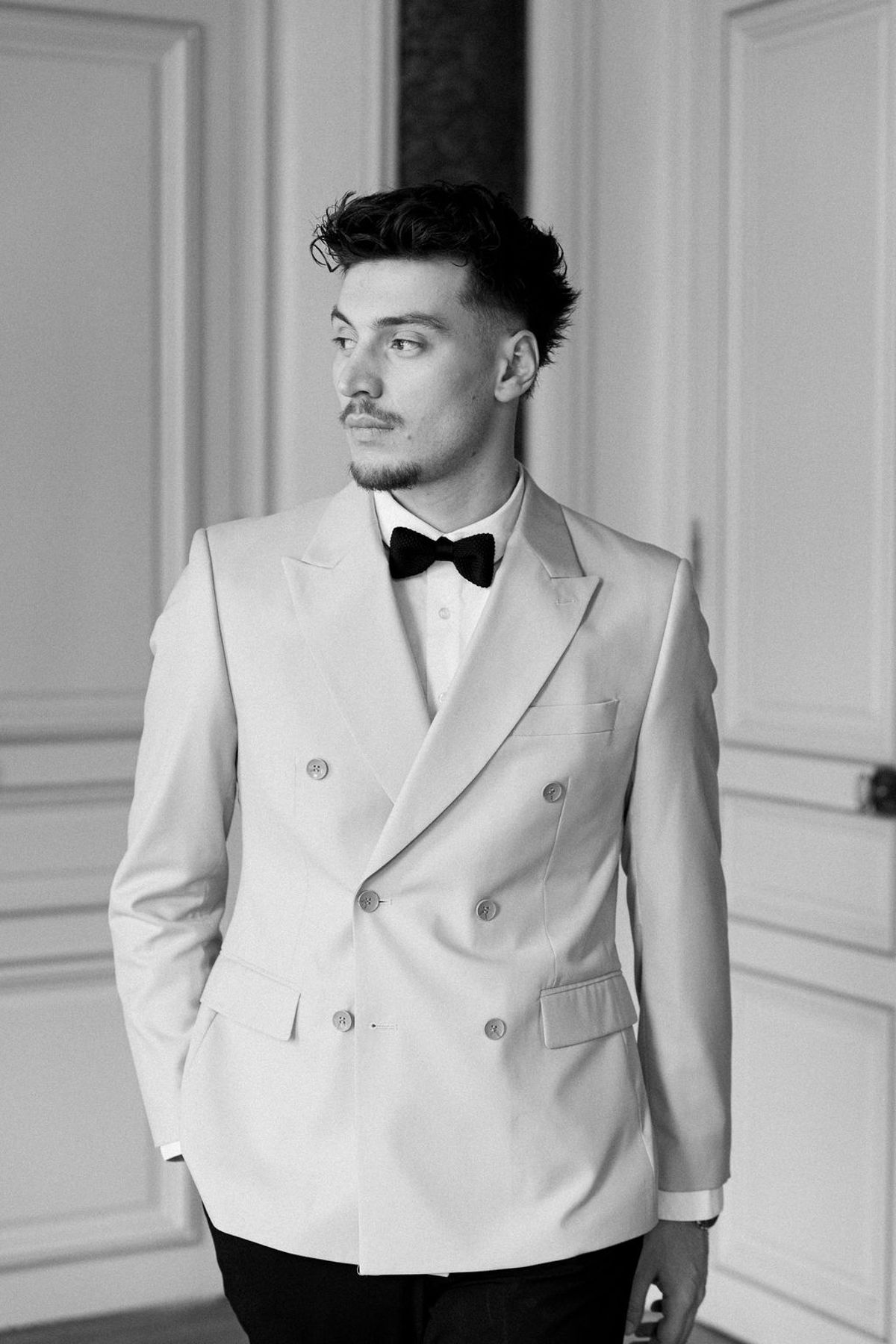 Groom in a pale dinner jacket looking to one side, photographed in black and white