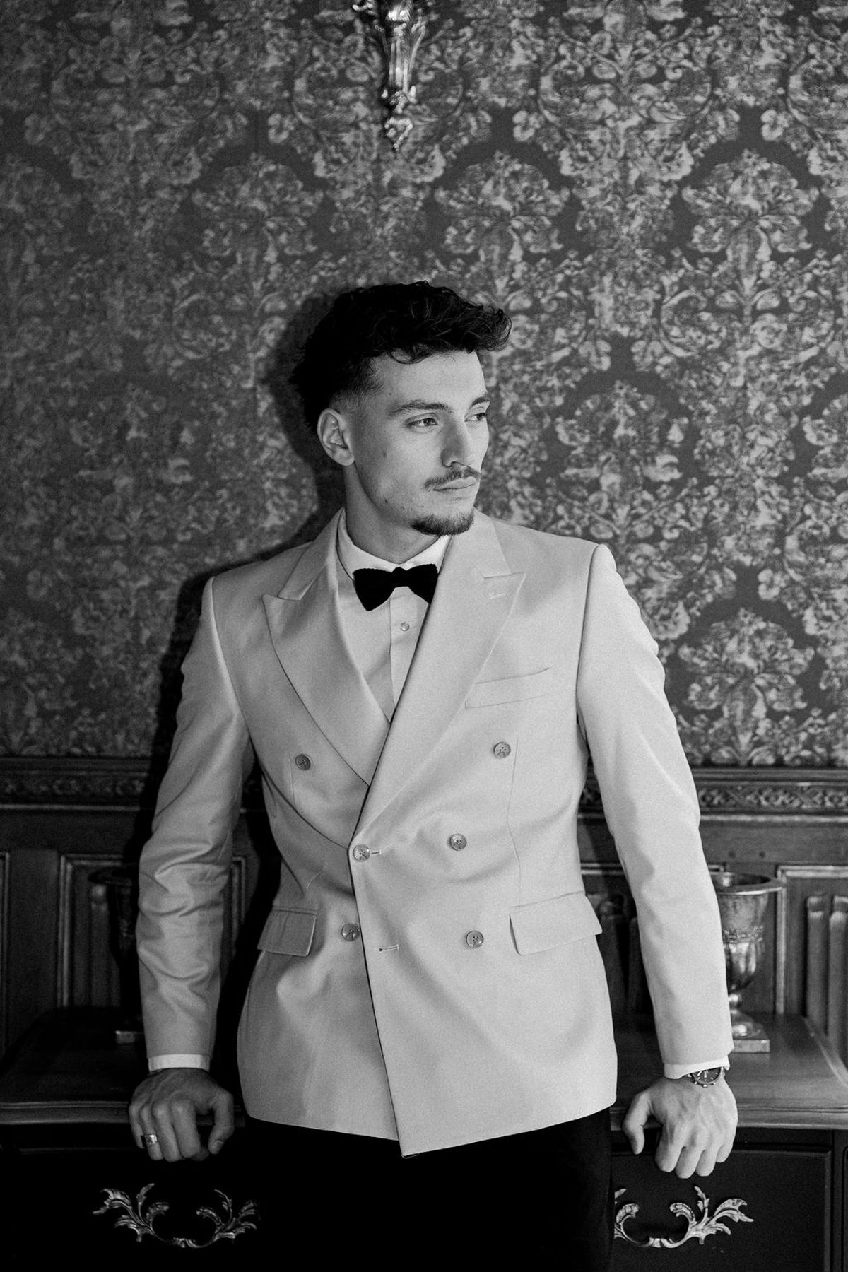 Groom in a pale double-breasted dinner jacket and black bow tie, photographed in black and white