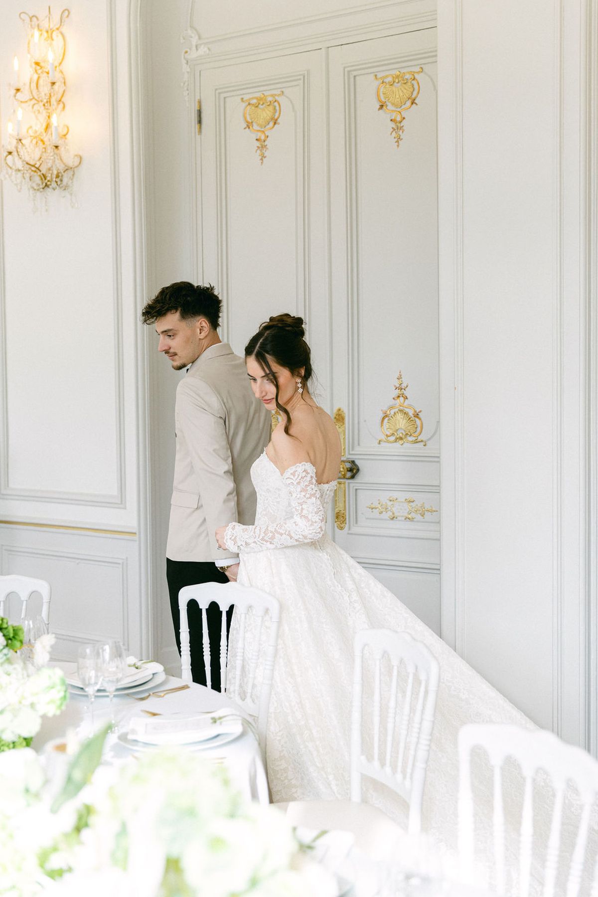 Couple standing beside the laid reception table in a chateau salon