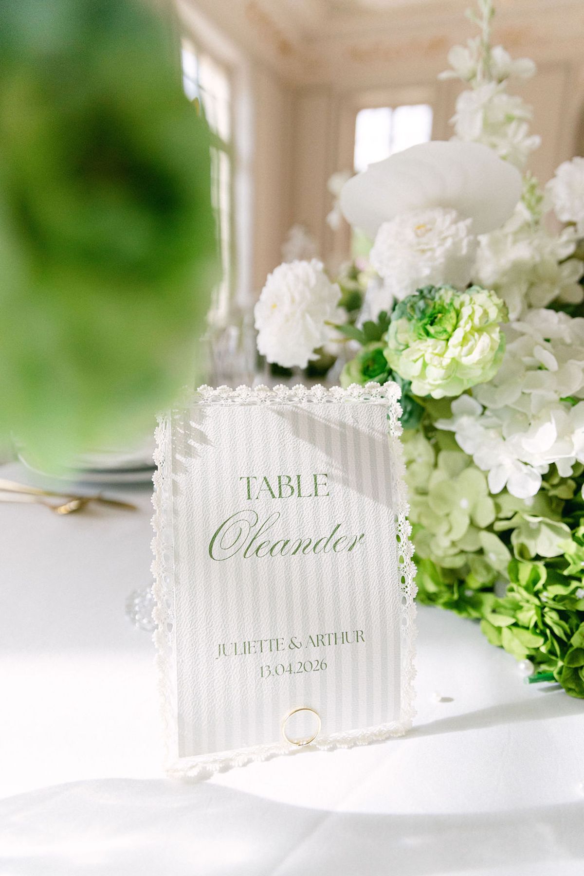 Table name card in a fluted white frame beside white roses and green hydrangea