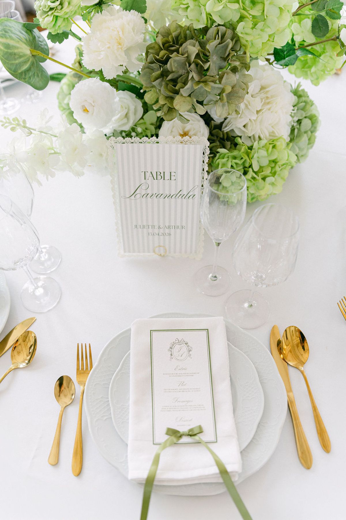 Place setting from above with gold cutlery, a menu card and white and green florals