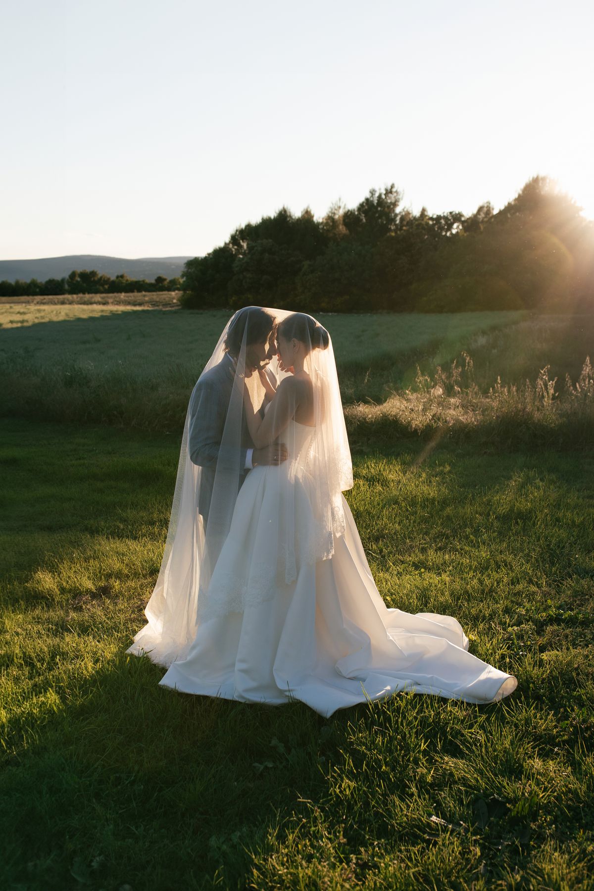 Bride and groom embracing under her veil at golden hour