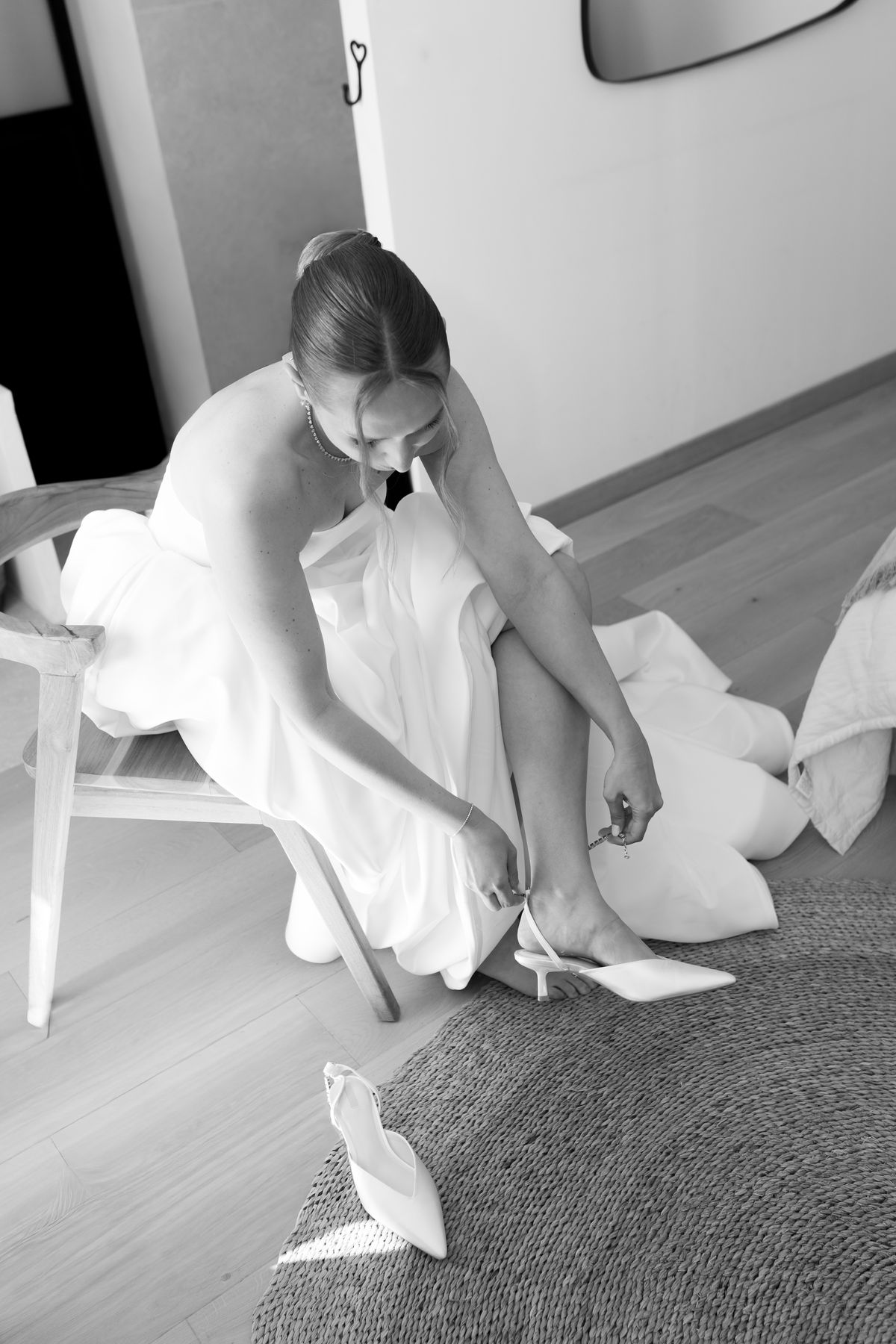 Bride sitting and adjusting her shoe, veil draped beside her