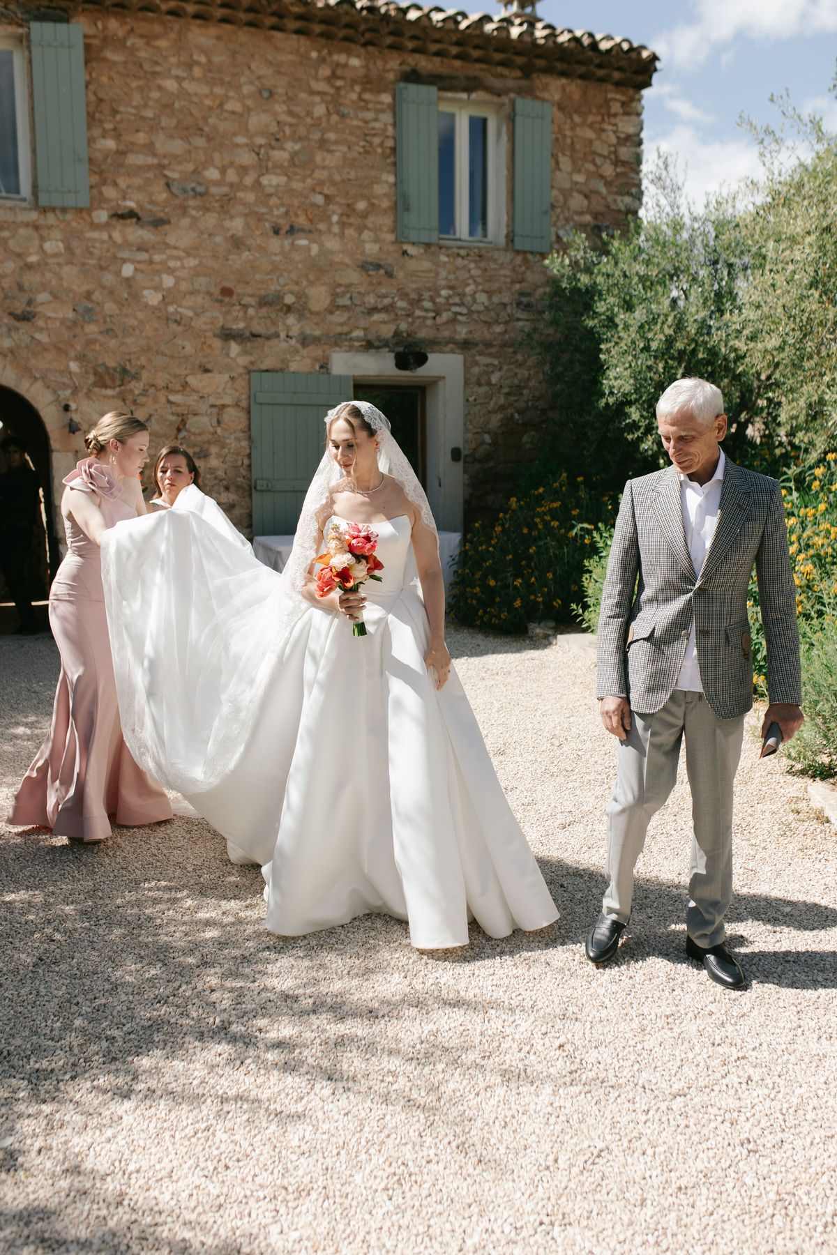 Bride walking with her parent and bridesmaid holding her train