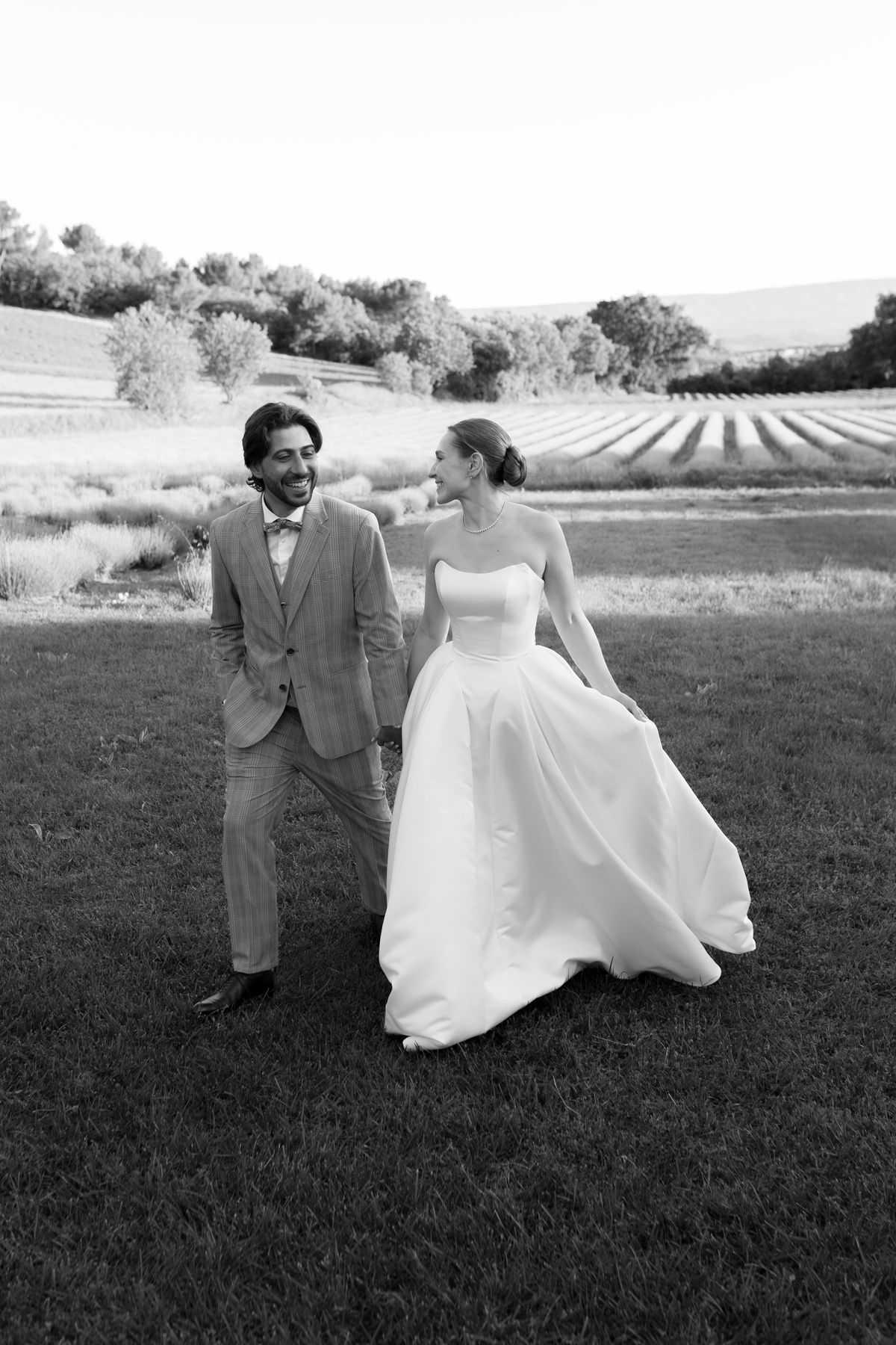 Bride and groom laughing together while walking through a field, black and white