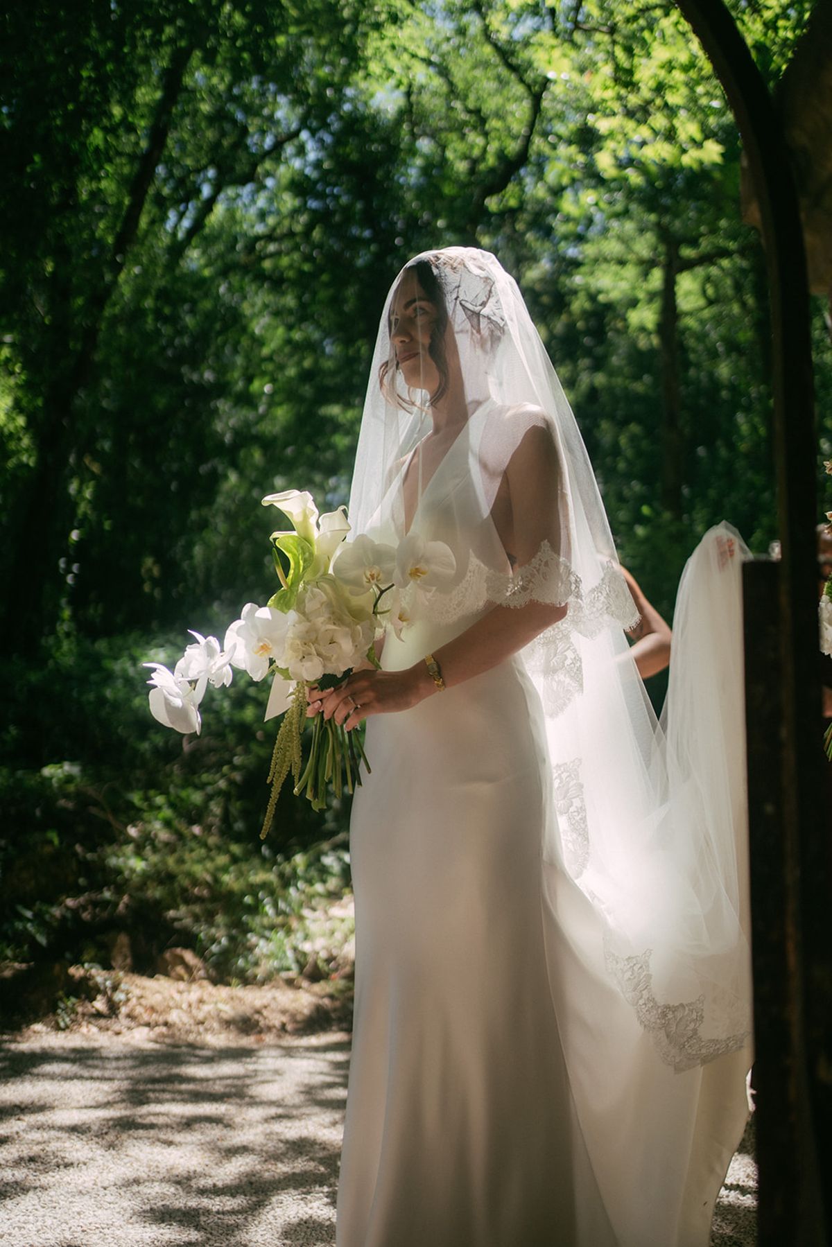 The bride with her bouquet in dappled woodland at Chateau du Pont Bourguet